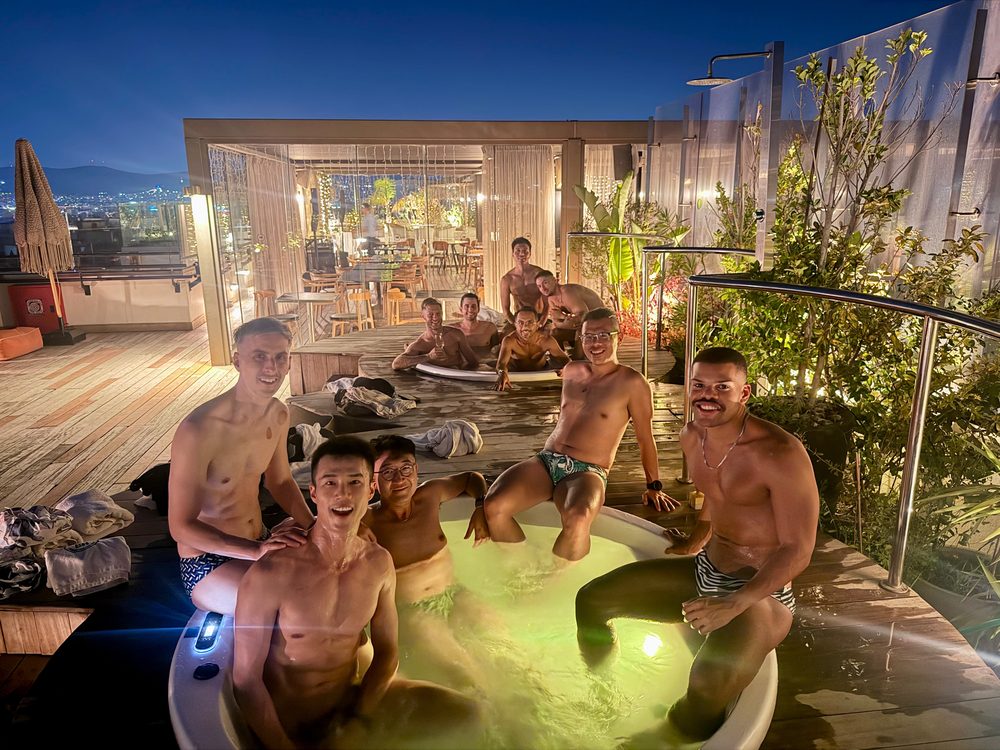 The group in a rooftop hot tub at night, drinks in hand