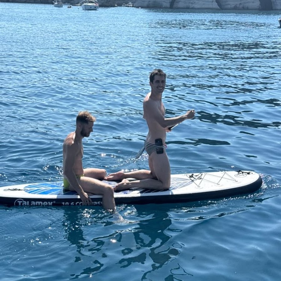 Two of the group out on a paddleboard in a cove, the boats anchored behind
