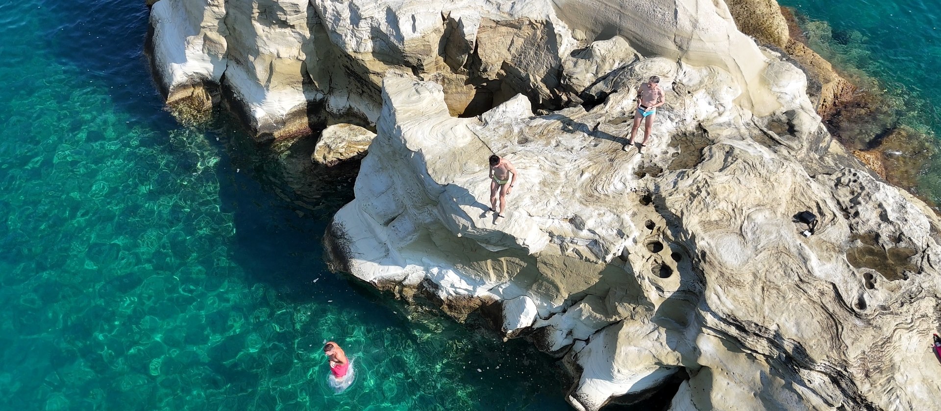 Three of the group on white rock above clear water, seen from above